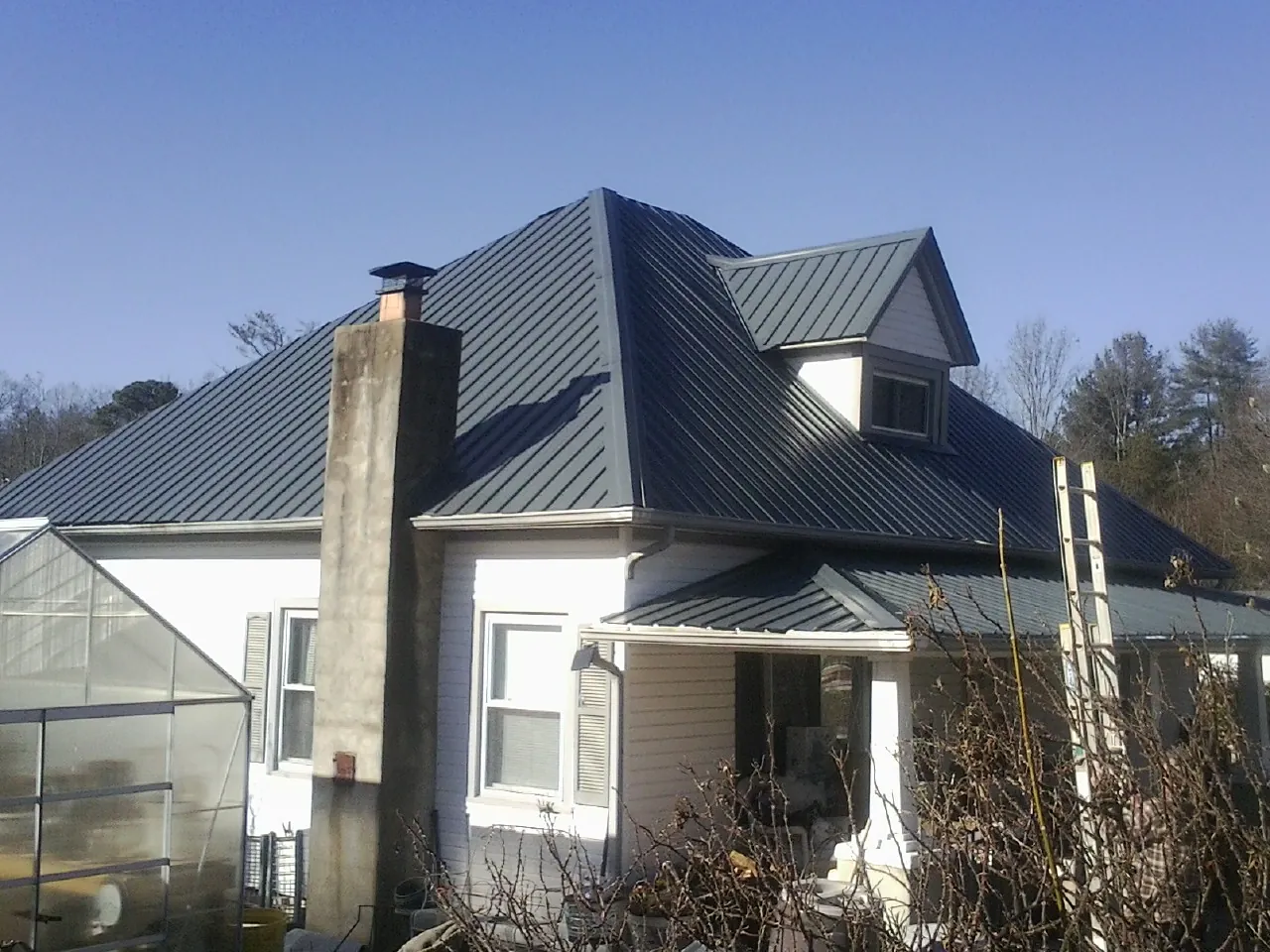 Dark blue standing seam metal roof on a white farmhouse with dormer — Slate & Tile Roof Repair by Roofing Brothers in Cedar Lane