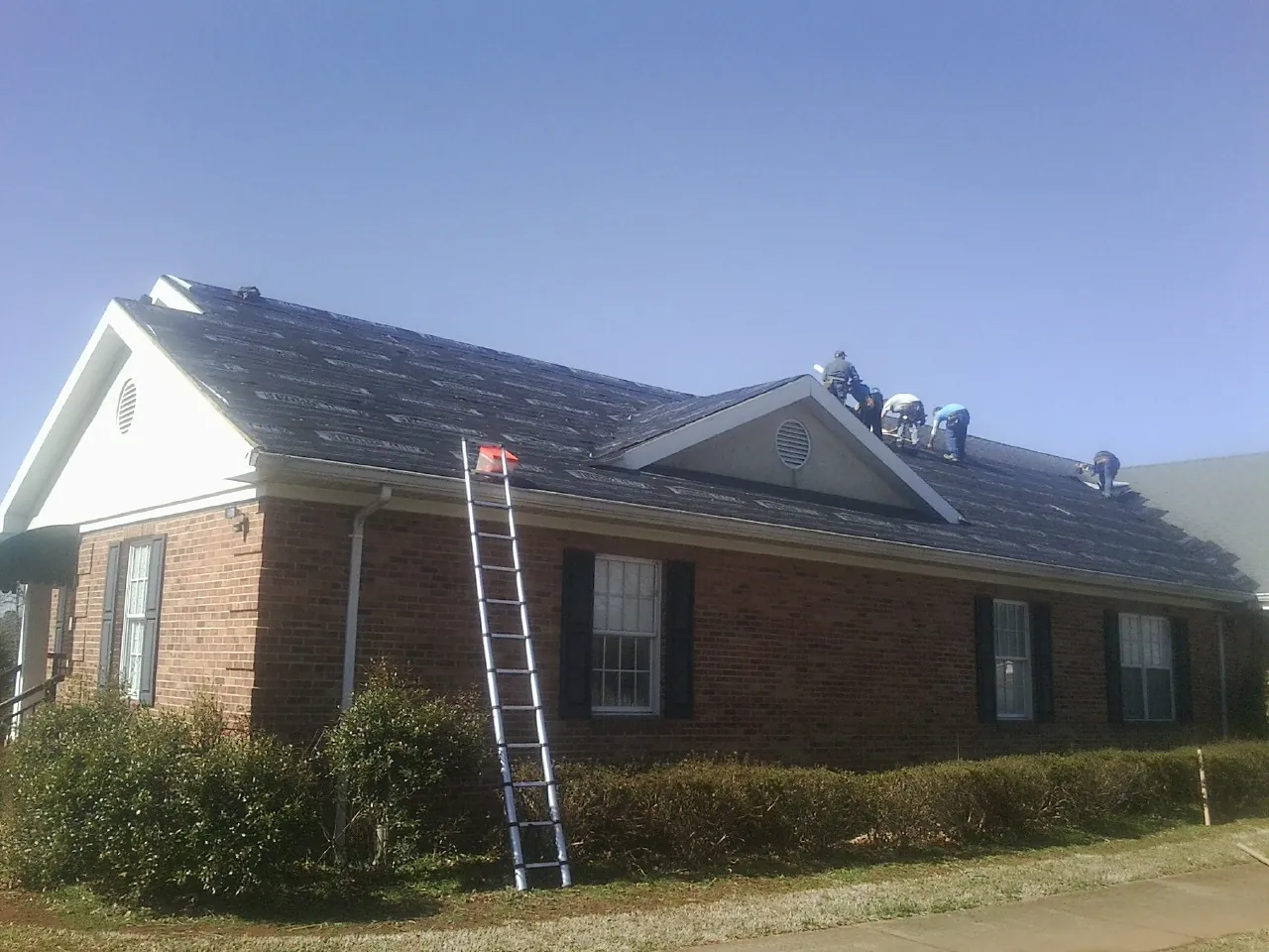Crew tearing shingles off a brick ranch roof with a ladder set — Metal Roof Repair work by our crew in Cedar Lane