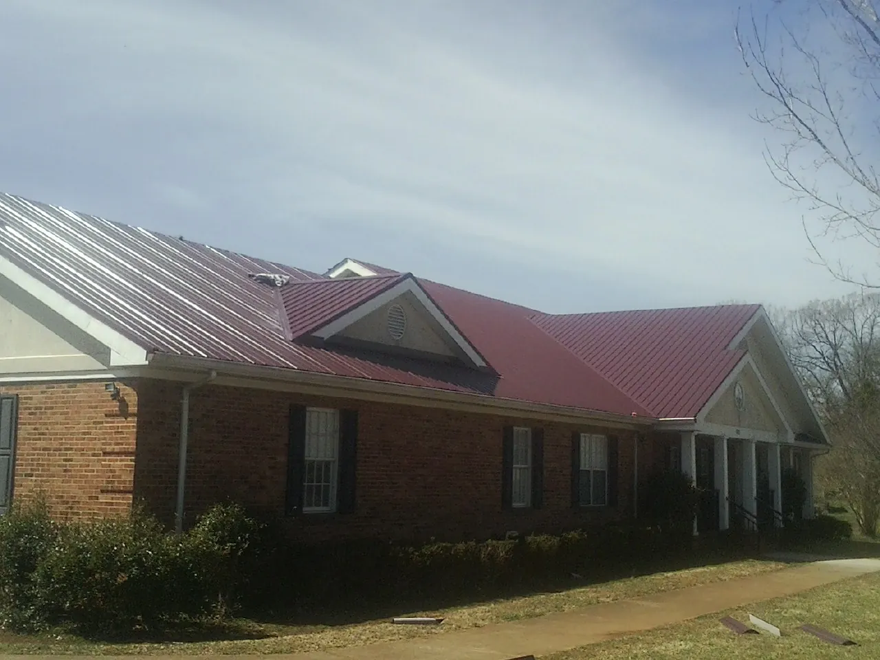 Red metal roof with gabled entries on a long brick building, from a Hail Damage Roof Repair job in Cedar Lane