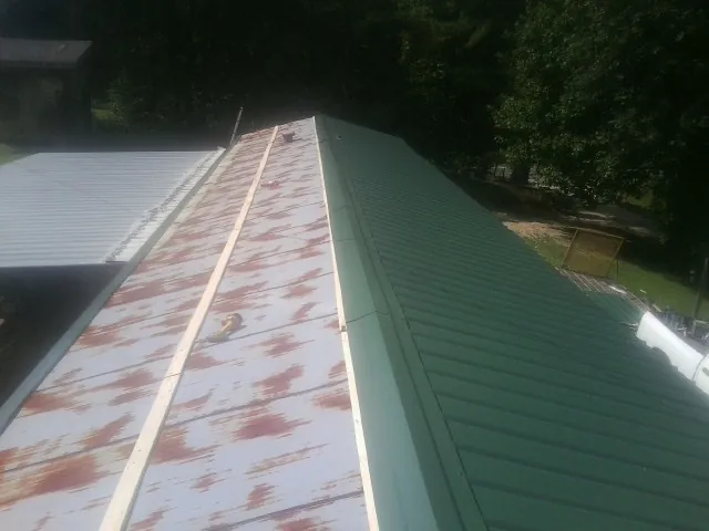 Old rusted panels beside newly installed green metal roofing — Wind Damage Roof Repair by Roofing Brothers in Cedar Lane