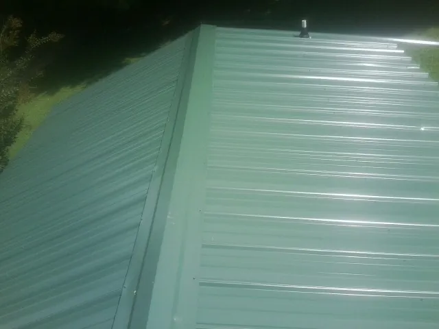 New green metal panels meeting at the ridge of a roof — Flat Roof Repair work by our crew in Cedar Lane