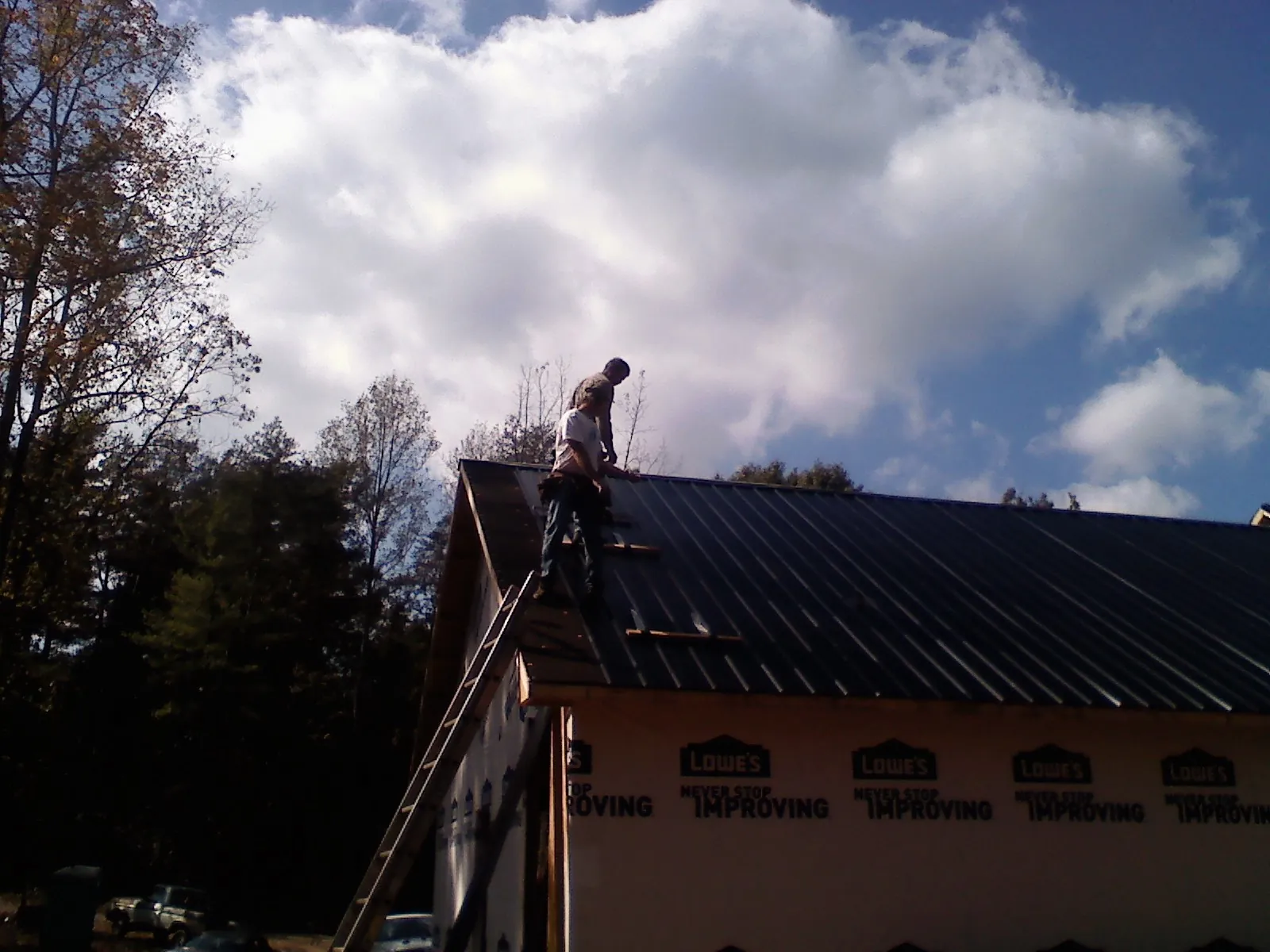 Roofer fastening dark metal panels high against a cloudy sky, from a Roof Inspection job in Cedar Lane