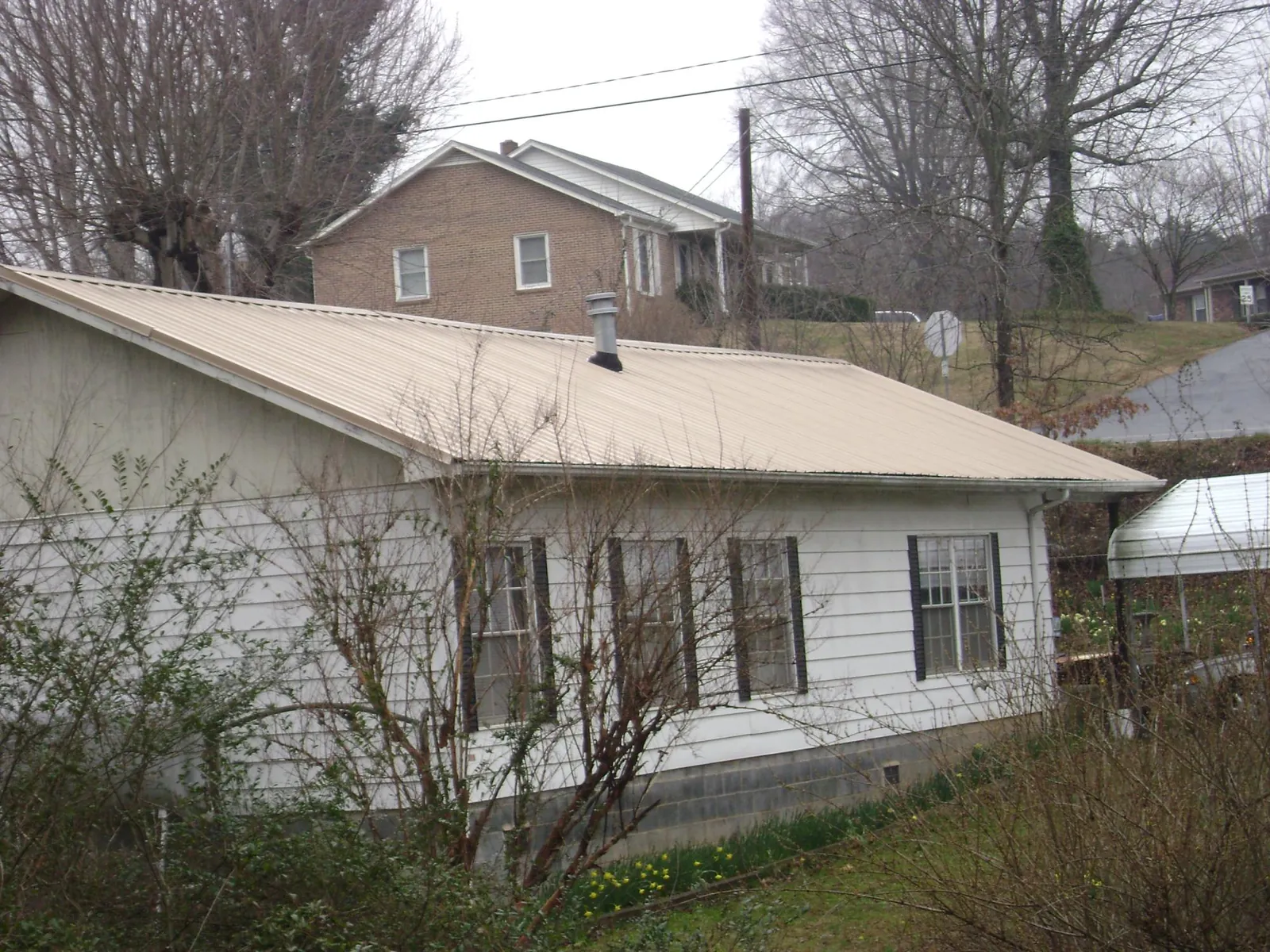 Tan metal roof on a white sided house set into a hillside — Commercial Roofing by Roofing Brothers in Cedar Lane