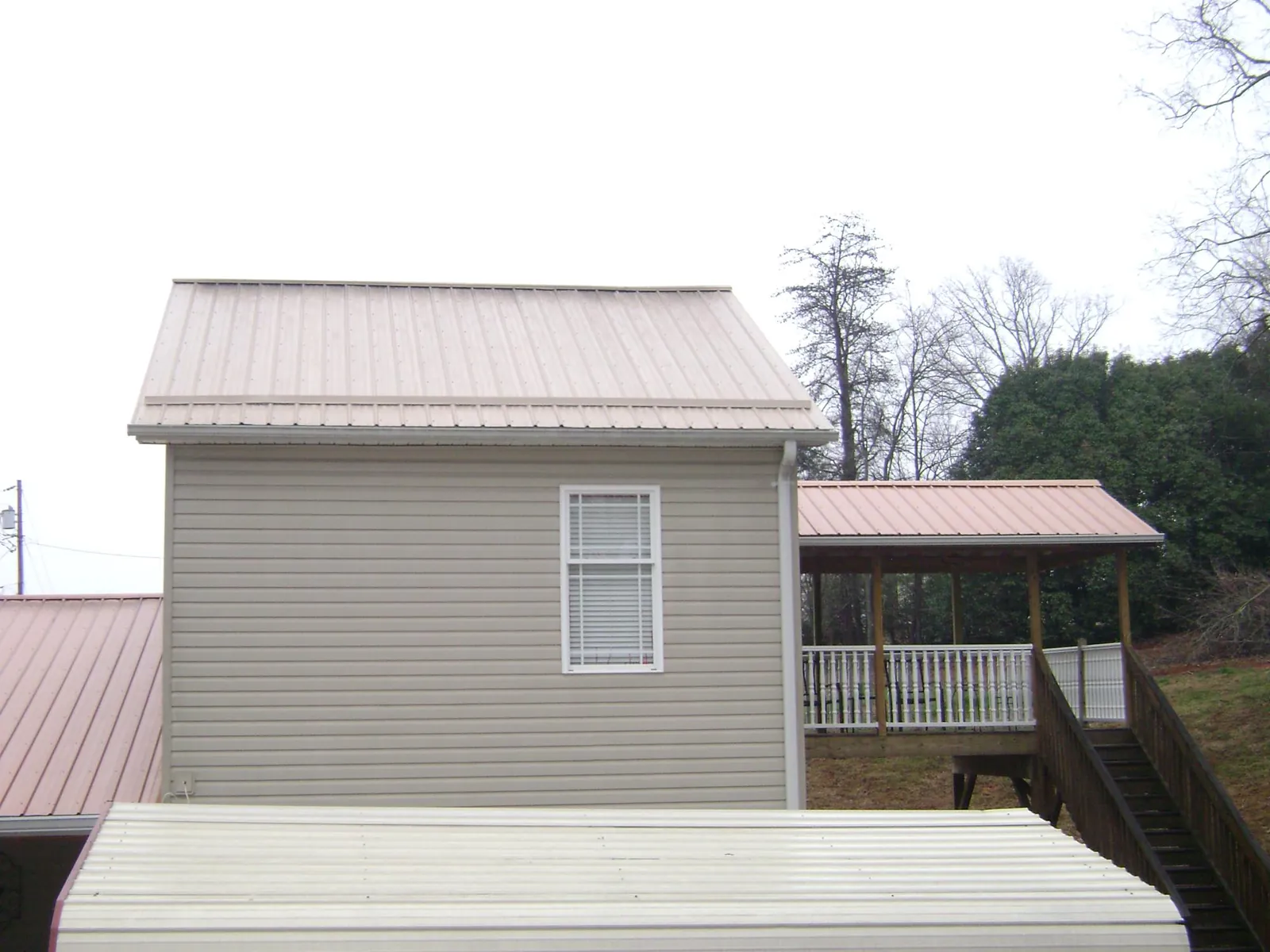Tan metal roofs on a two story addition and attached porch, from a Roof Replacement job in Cedar Lane